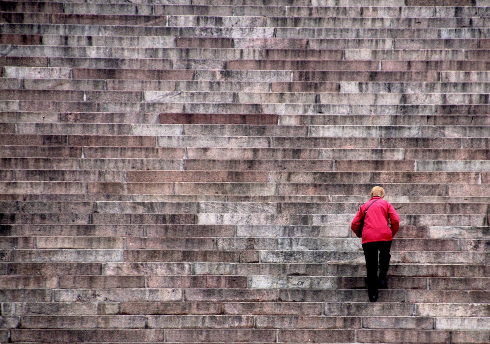 A person in a red jacket climbing massive stone stairs, symbolizing challenge and effort.