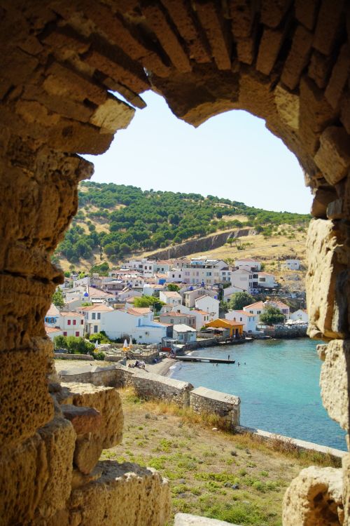 Free A charming coastal village viewed through ancient stone ruins overlooking the sea. Stock Photo