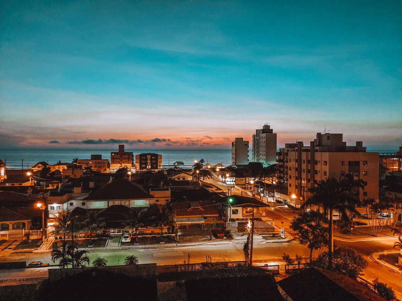A beautiful cityscape view of Matinhos in Brazil at dusk, showcasing illuminated buildings against a vibrant sky.