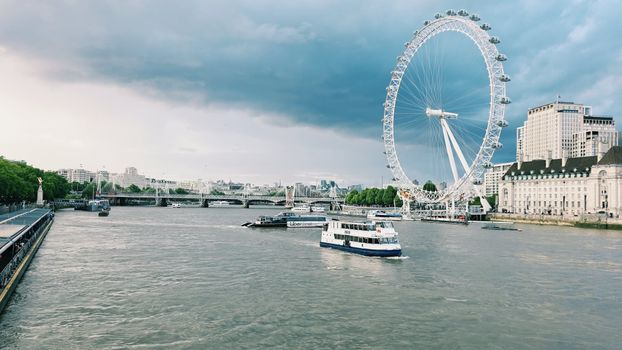Captivating view of the London Eye and River Thames with boats on a cloudy day in London.