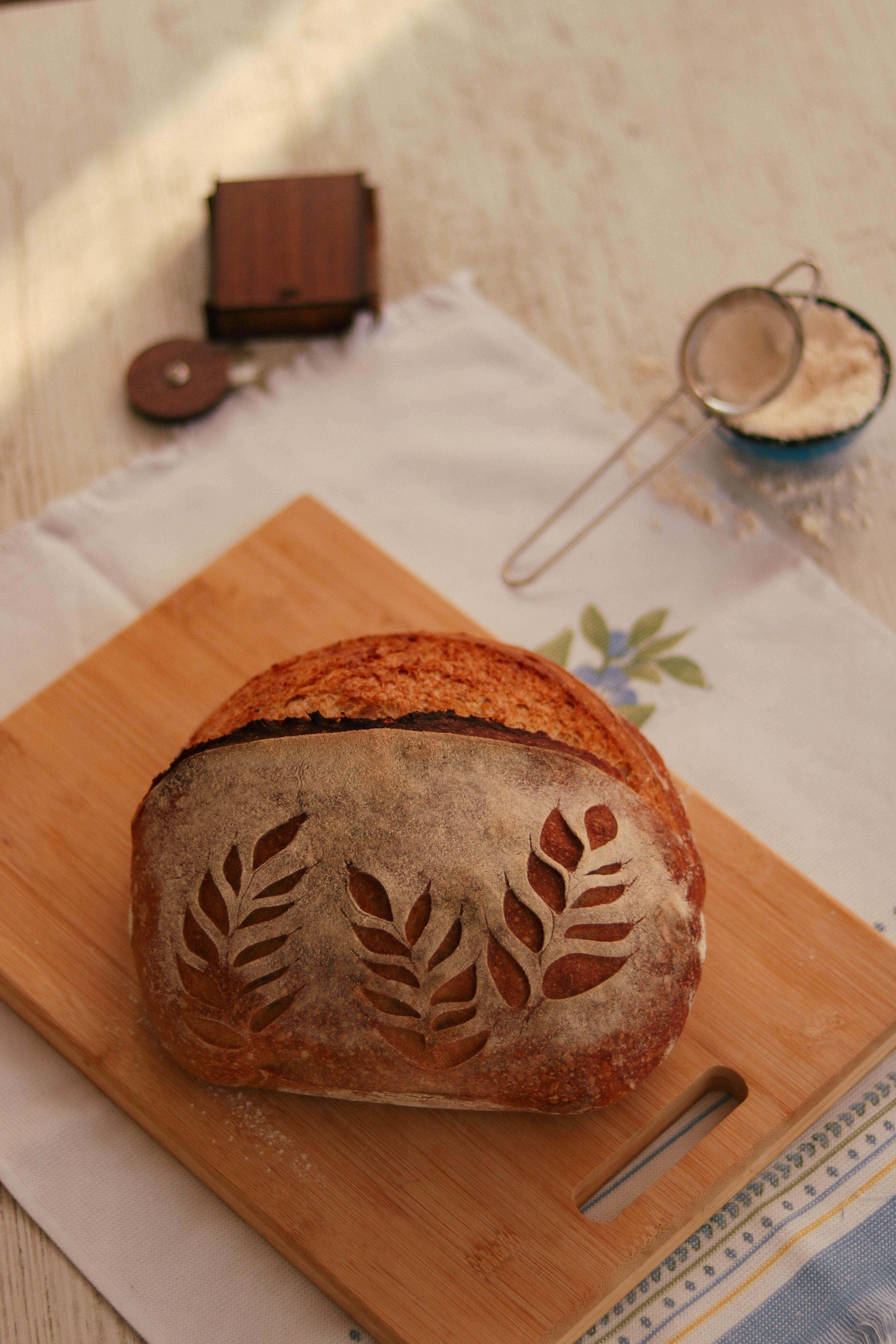 Scored whole-grain loaf on a board beside a flour sieve — photo by Feyza Daştan on Pexels