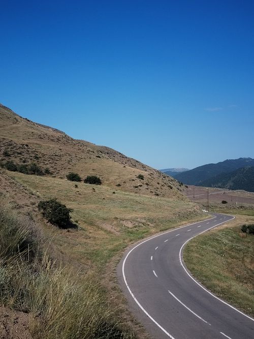 Free A serene view of a winding road through a mountain landscape under a clear blue sky. Stock Photo