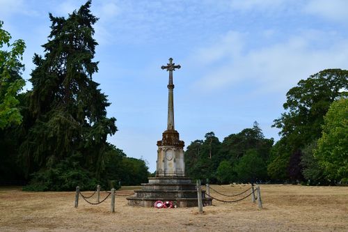 Free A stone memorial with a cross stands in a serene park surrounded by lush trees under a clear sky. Stock Photo