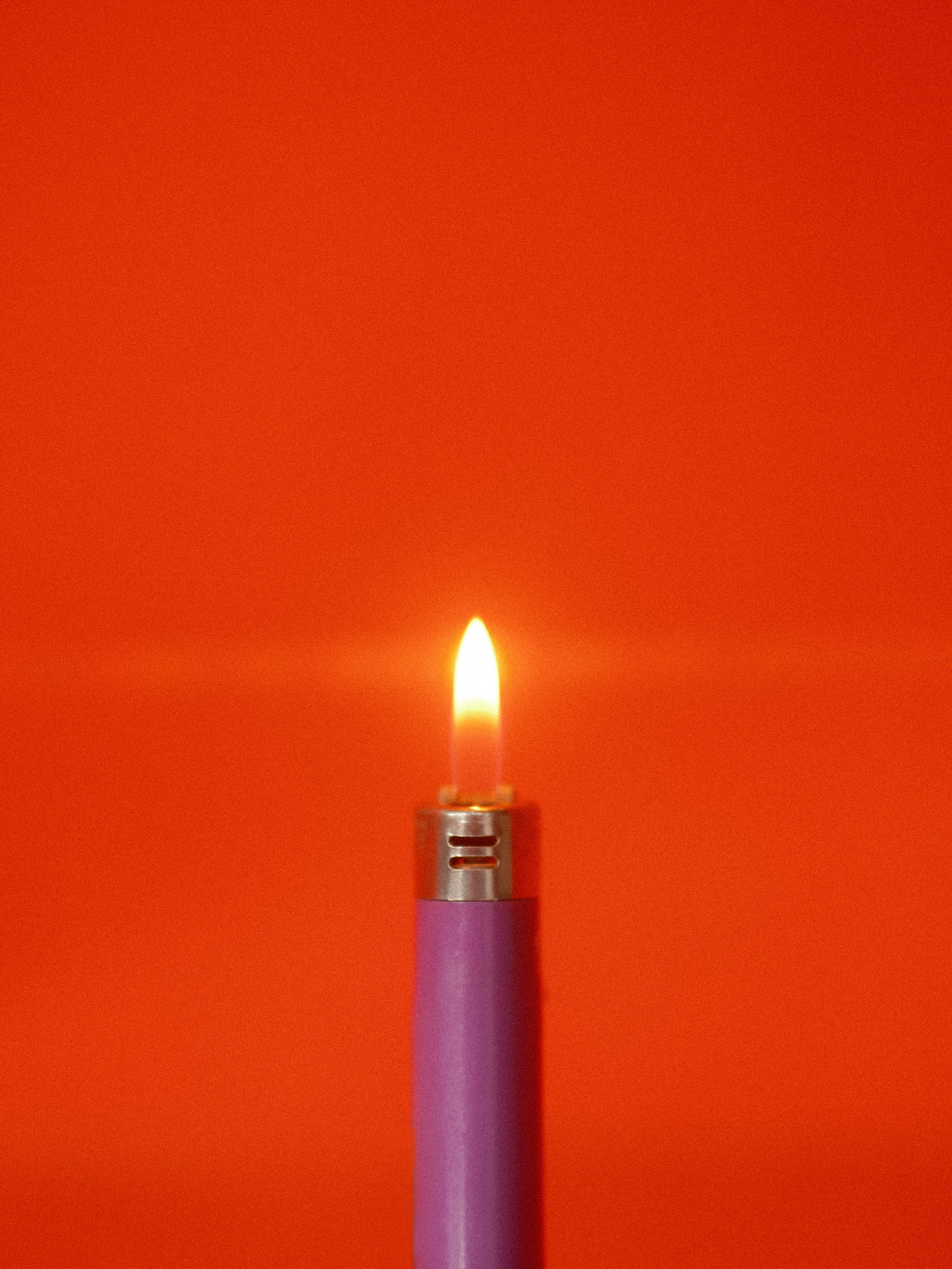 Close-up of a purple lighter with a flame, set against a red background.