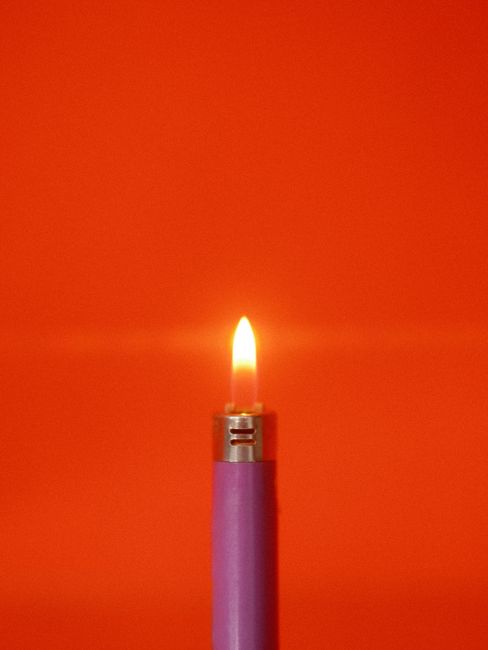 Close-up of a purple lighter with a flame, set against a red background.