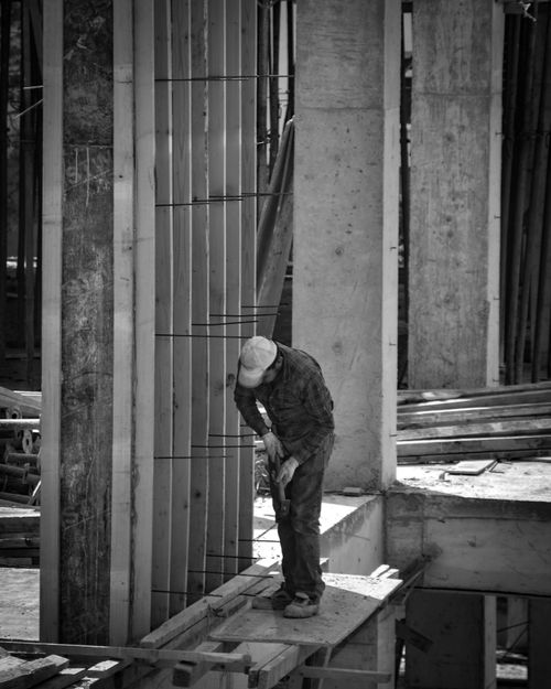 Free Black and white photo of a construction worker at a building site, emphasizing structure. Stock Photo