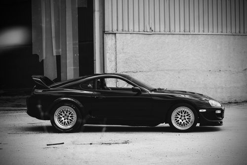 Free Black sports car parked in front of an industrial building, showcasing sleek design and performance. Stock Photo