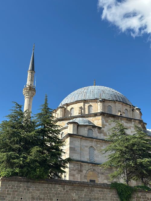Free A beautiful historic mosque featuring a towering minaret surrounded by green trees under a clear blue sky. Stock Photo