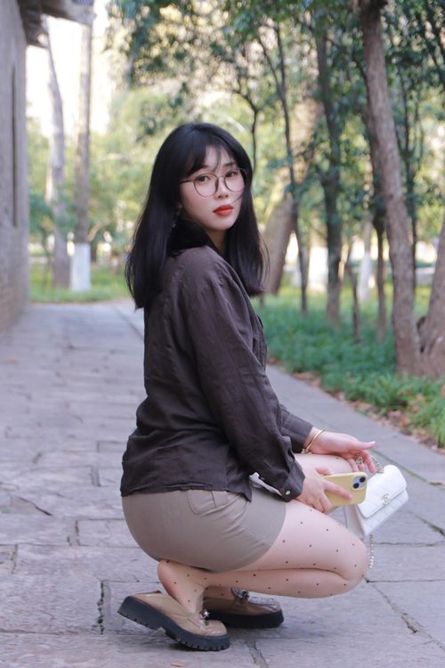 Free Portrait of a young woman squatting outdoors in Nanjing, China, wearing fashionable attire. Stock Photo