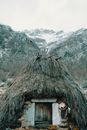 Old aboriginal stone wigwam with thatched roof located on snowy mountainous terrain in winter