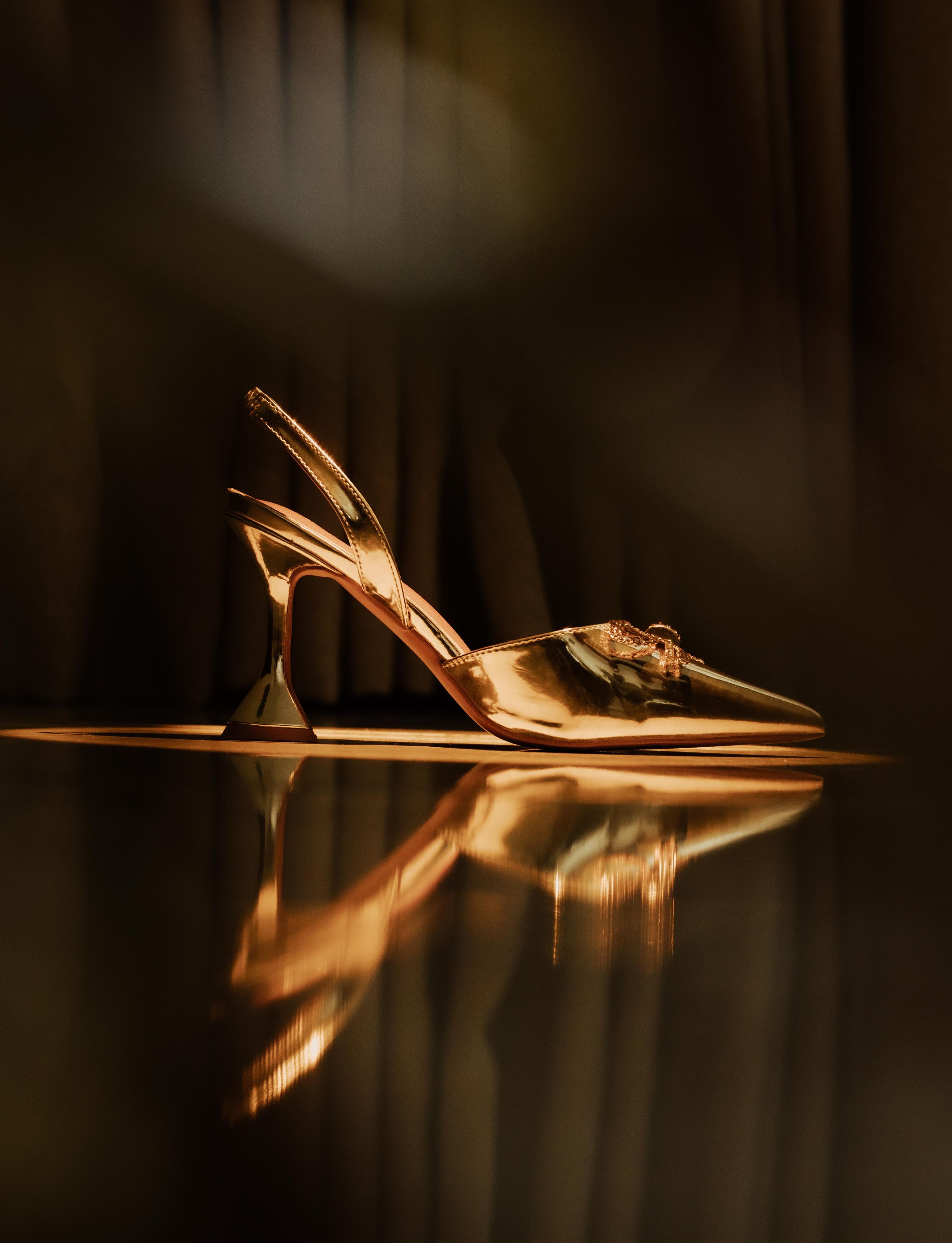 Um luxuoso sapato de salto alto dourado com superfície refletora e iluminação elegante.