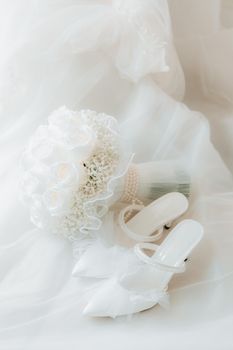 A sophisticated flat lay of white bridal shoes paired with a delicate bouquet on a soft fabric.
