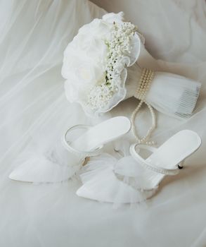 A flat lay of bridal shoes and a white bouquet with pearls, perfect for a wedding.