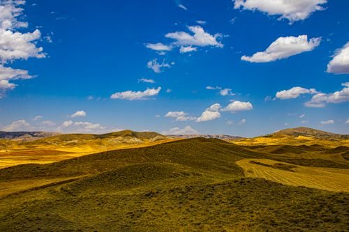 Free Beautiful view of rolling hills and a bright blue sky with scattered clouds, captured during a sunny day. Stock Photo