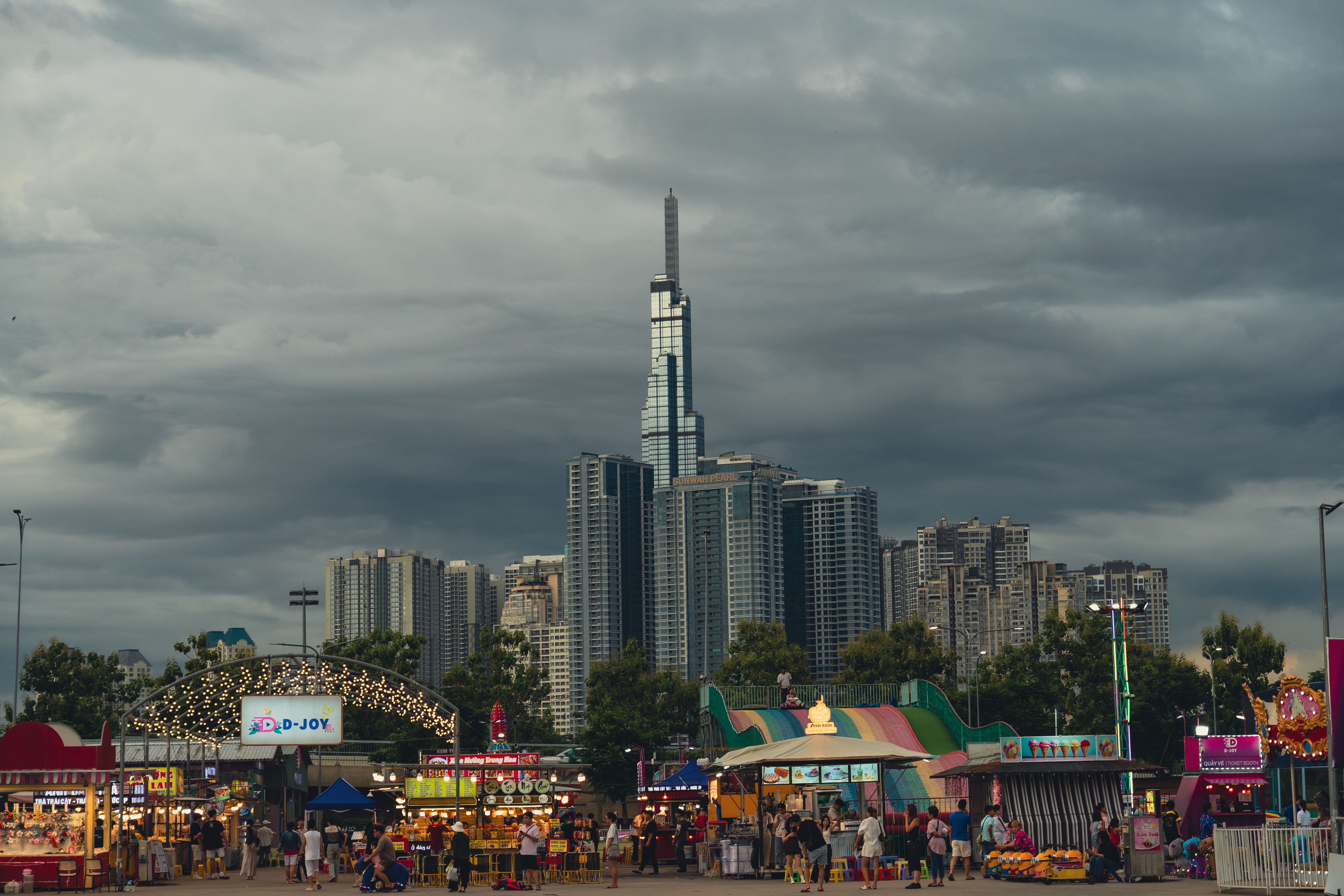 Vibrant carnival scene with tall modern skyscrapers under cloudy sky.