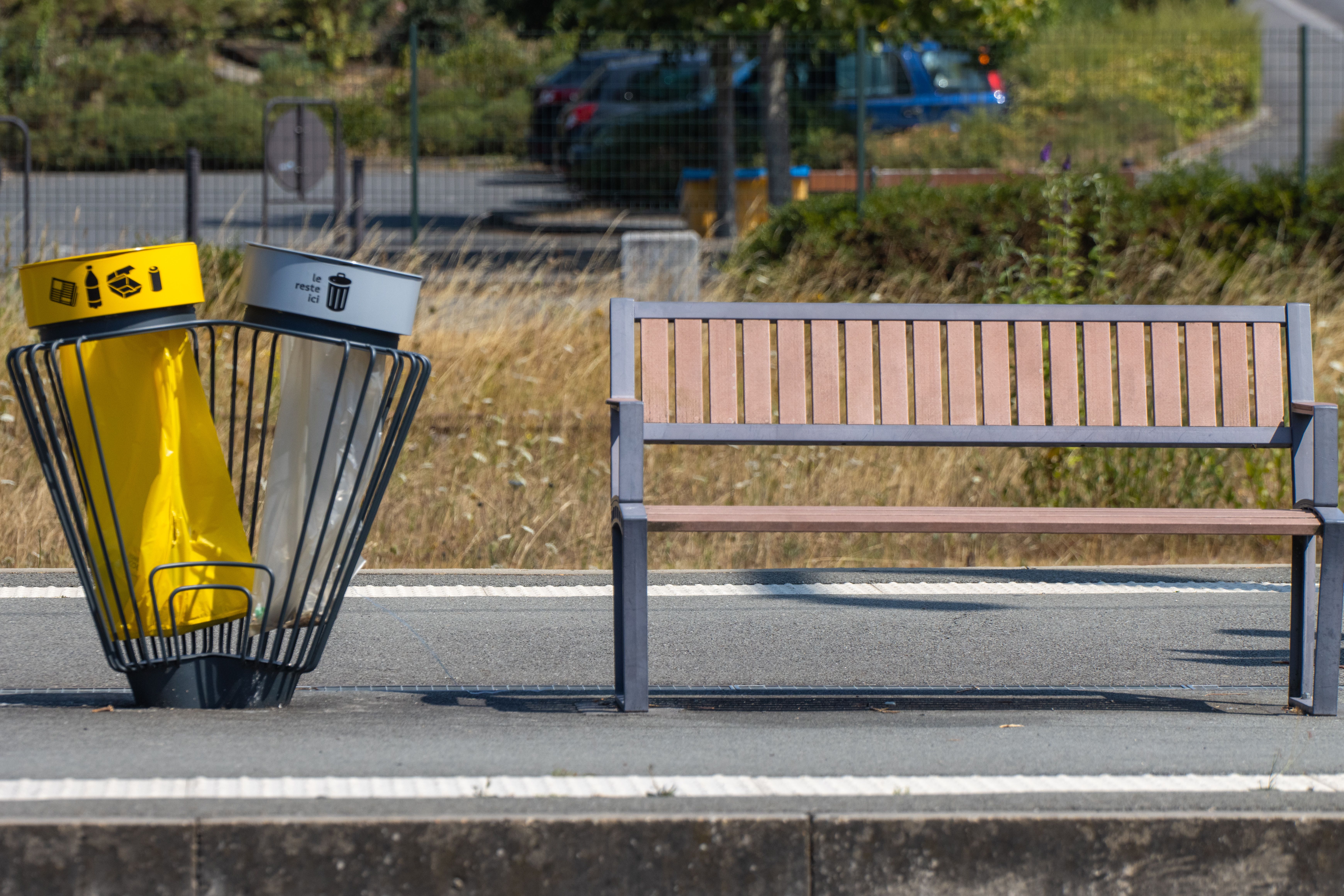 A wooden bench and recycling bin on a sunny day in Dol-de-Bretagne, France.