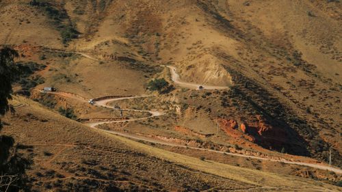 Free A winding dirt road traverses scenic arid hills under a clear sky, with sparse vegetation. Stock Photo