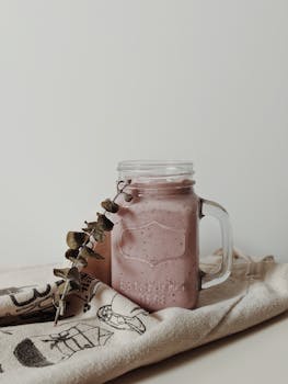 A rustic smoothie in a mason jar with eucalyptus on a decorative cloth, ideal for food photography.