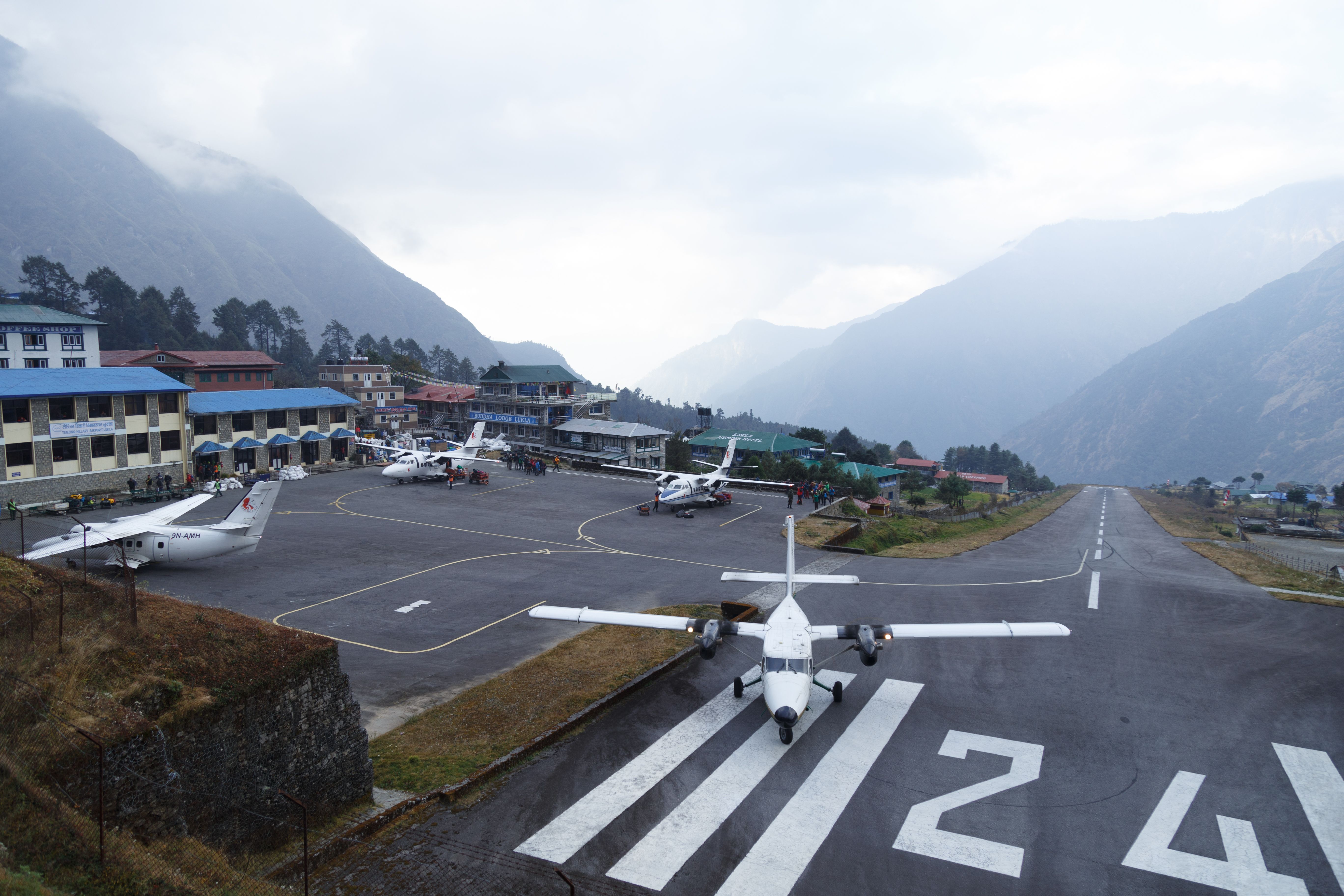Small aircraft on runway at Lukla Airport in the Himalayas, surrounded by mountains and mist.