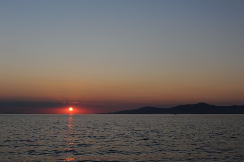 Free Beautiful sunset over the ocean with a serene horizon and distant mountains. Stock Photo