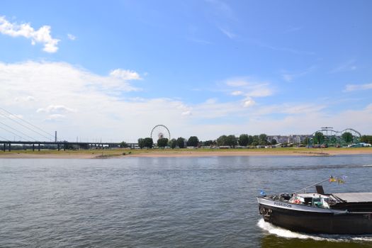 View of the Rhine River with a boat, ferris wheel, and cityscape in Düsseldorf, Germany.
