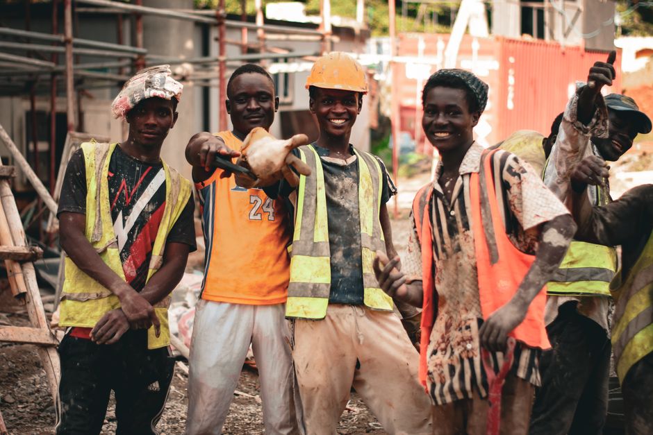 Group of smiling construction workers wearing safety vests and helmets on a construction site.