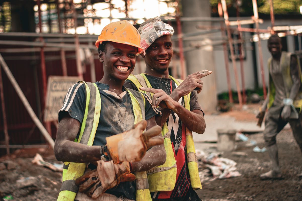 Two smiling construction workers in hard hats and safety vests pointing with joy