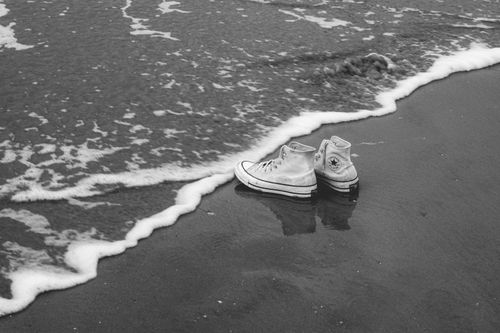 Free Monochrome image of sneakers reflecting on wet sand near ocean waves. Stock Photo