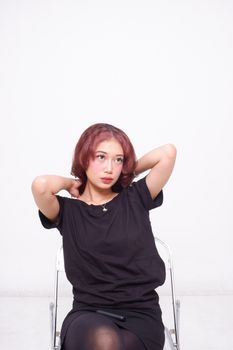 Portrait of a young woman with makeup posing on a chair in a minimalist studio setting.