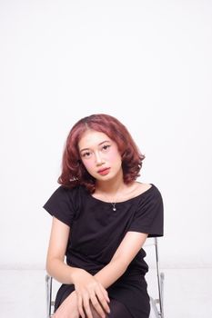 A young woman with red hair sitting on a chair against a plain white background.