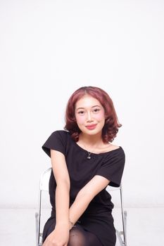 A young woman with short red hair sitting on a chair in a studio setting.