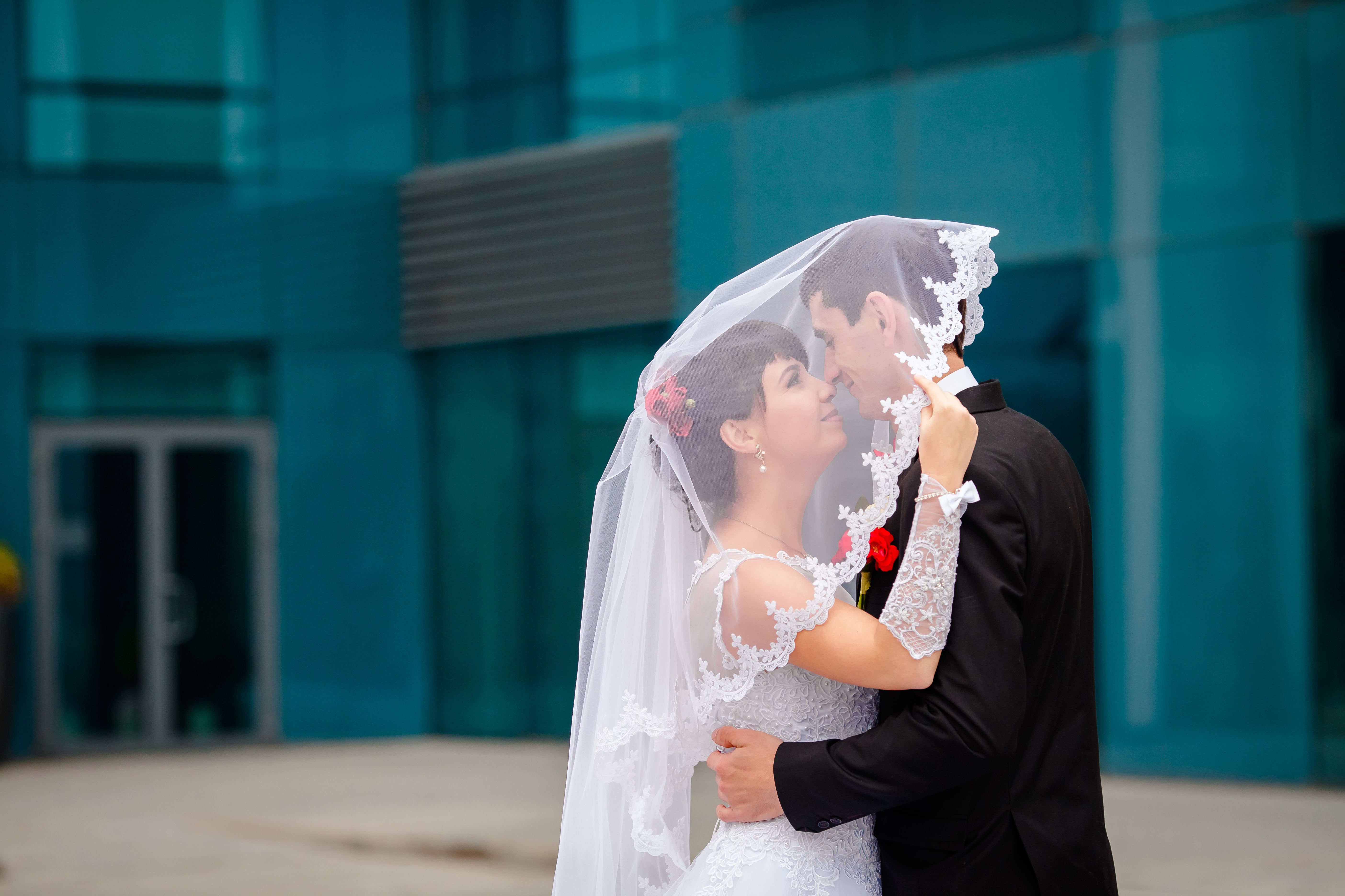 A bride and groom share a tender moment outdoors, embracing beneath a lace veil.