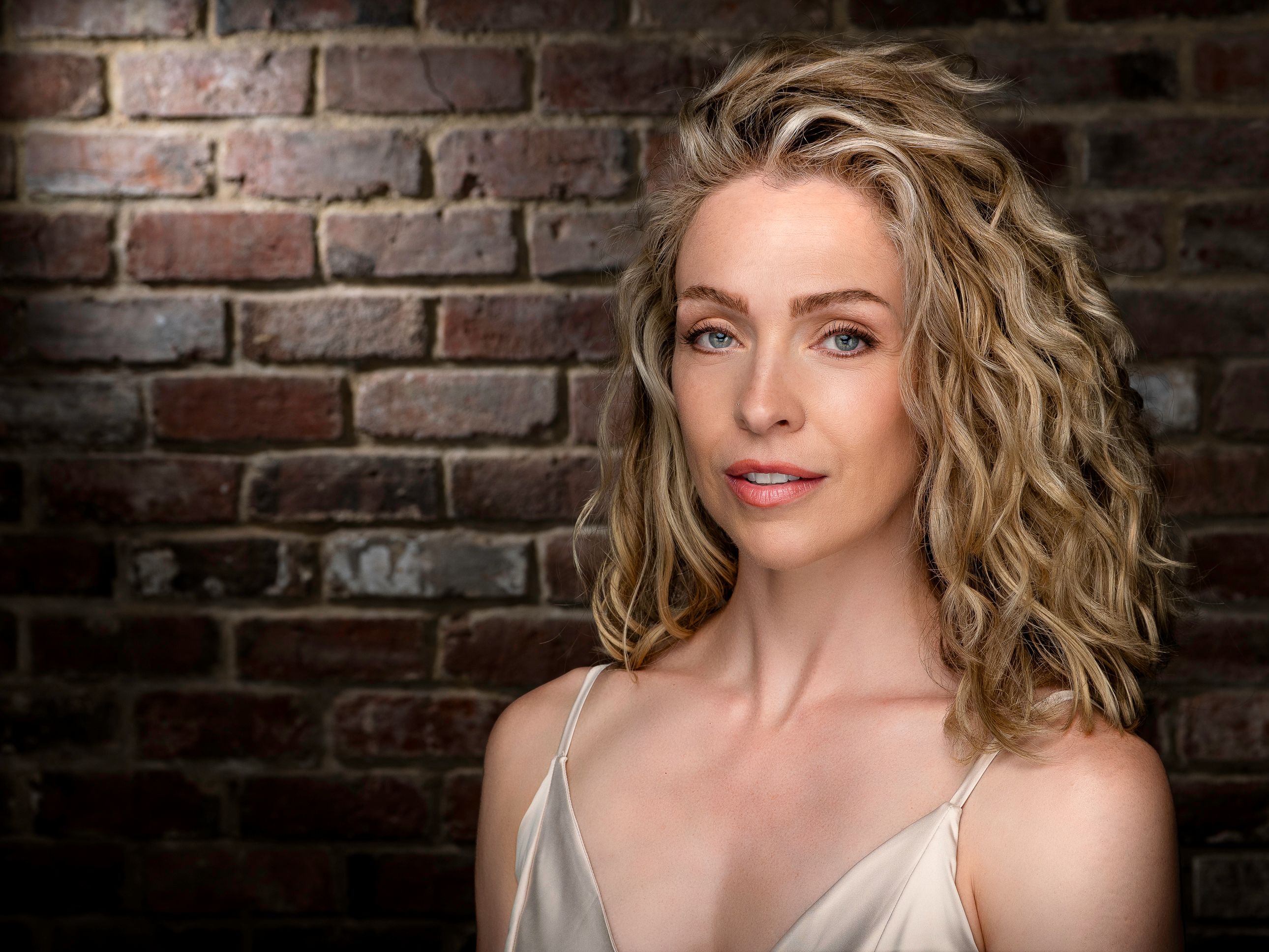 Elegant portrait of a woman with curly hair against a brick wall background.