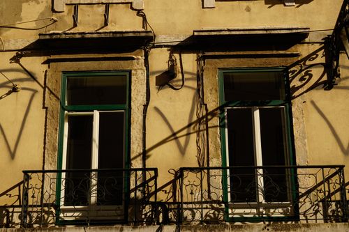 Free Charming Portuguese balcony with wrought iron details in warm sunlight, casting striking shadows. Stock Photo