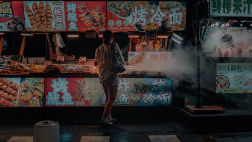 Free Vibrant night market scene with a person ordering from a steaming street food stall. Stock Photo