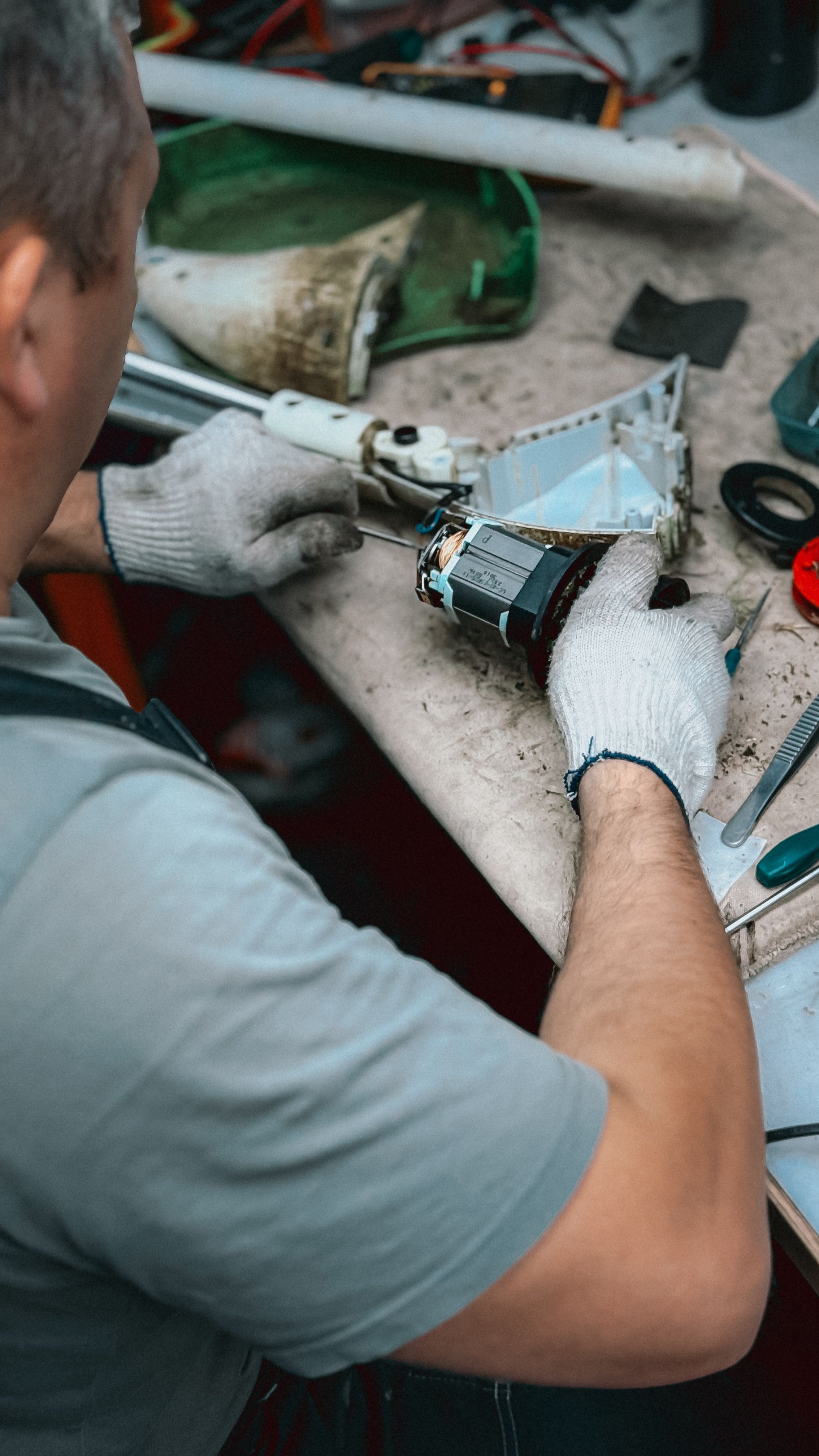 A technician wearing gloves fixes a small appliance on a cluttered workbench, focusing on intricate details.