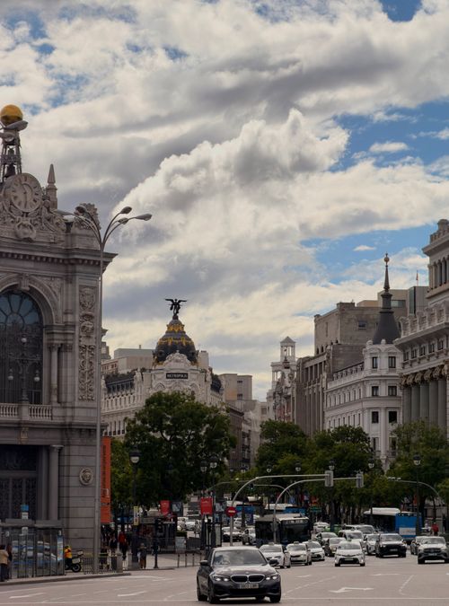 Free Scenic view of Madrid's Gran Via featuring Metropolis Building, busy street, and iconic architecture under cloudy skies. Stock Photo