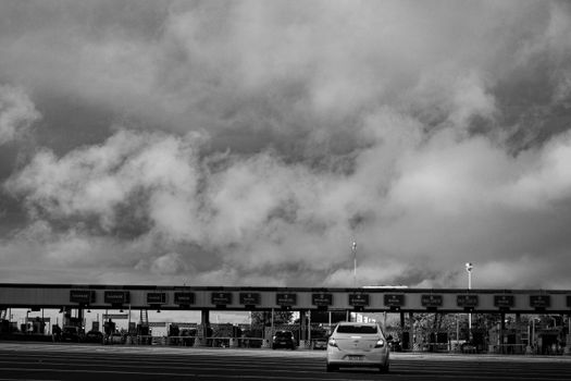 Monochrome view of a toll booth under dramatic clouded skies, featuring a lone car.