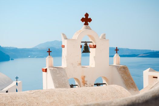Stunning view of a white church bell tower with cross, overlooking the Aegean Sea in Santorini, Greece.
