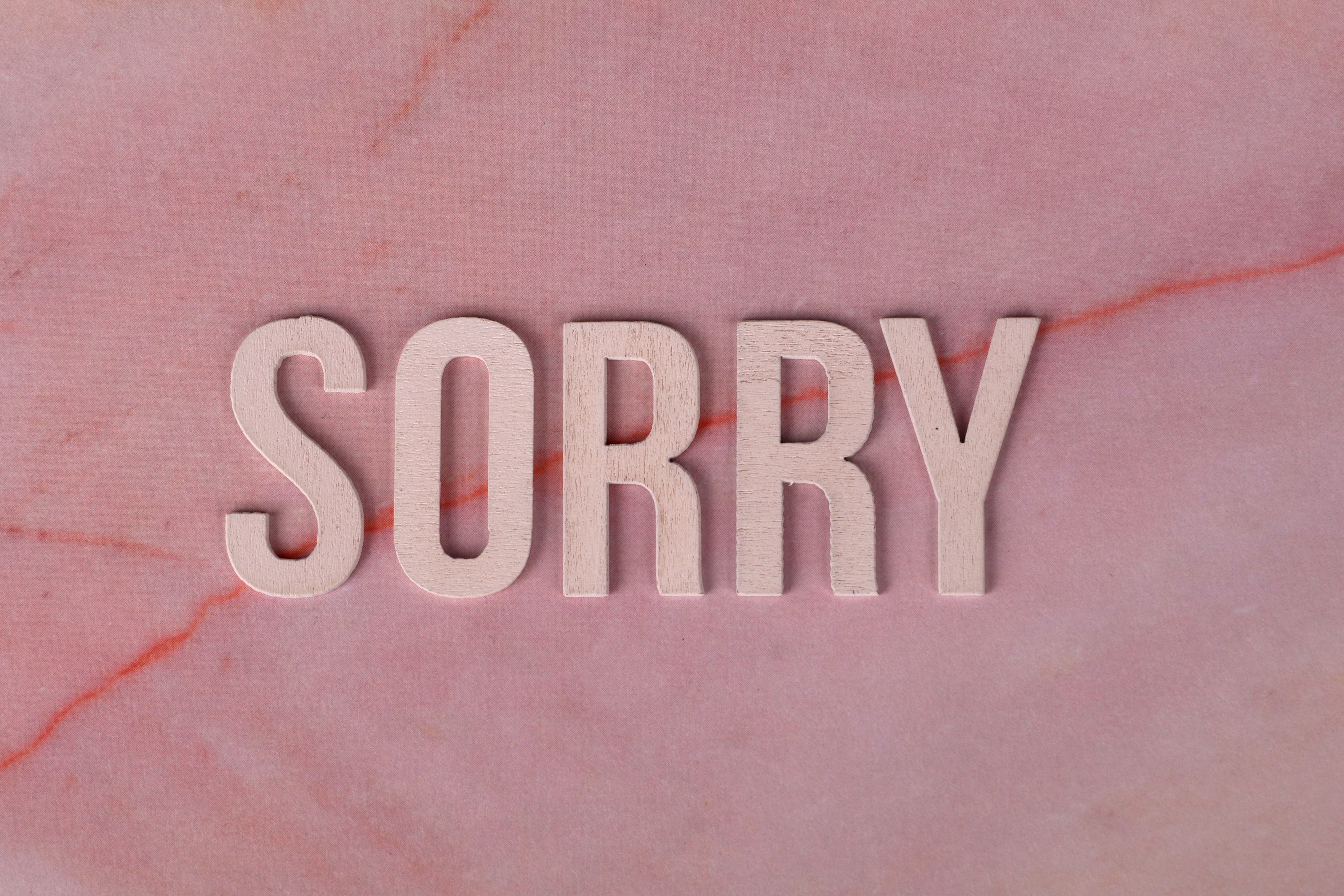Wooden letters spelling 'SORRY' on a pink marble surface, apology concept.