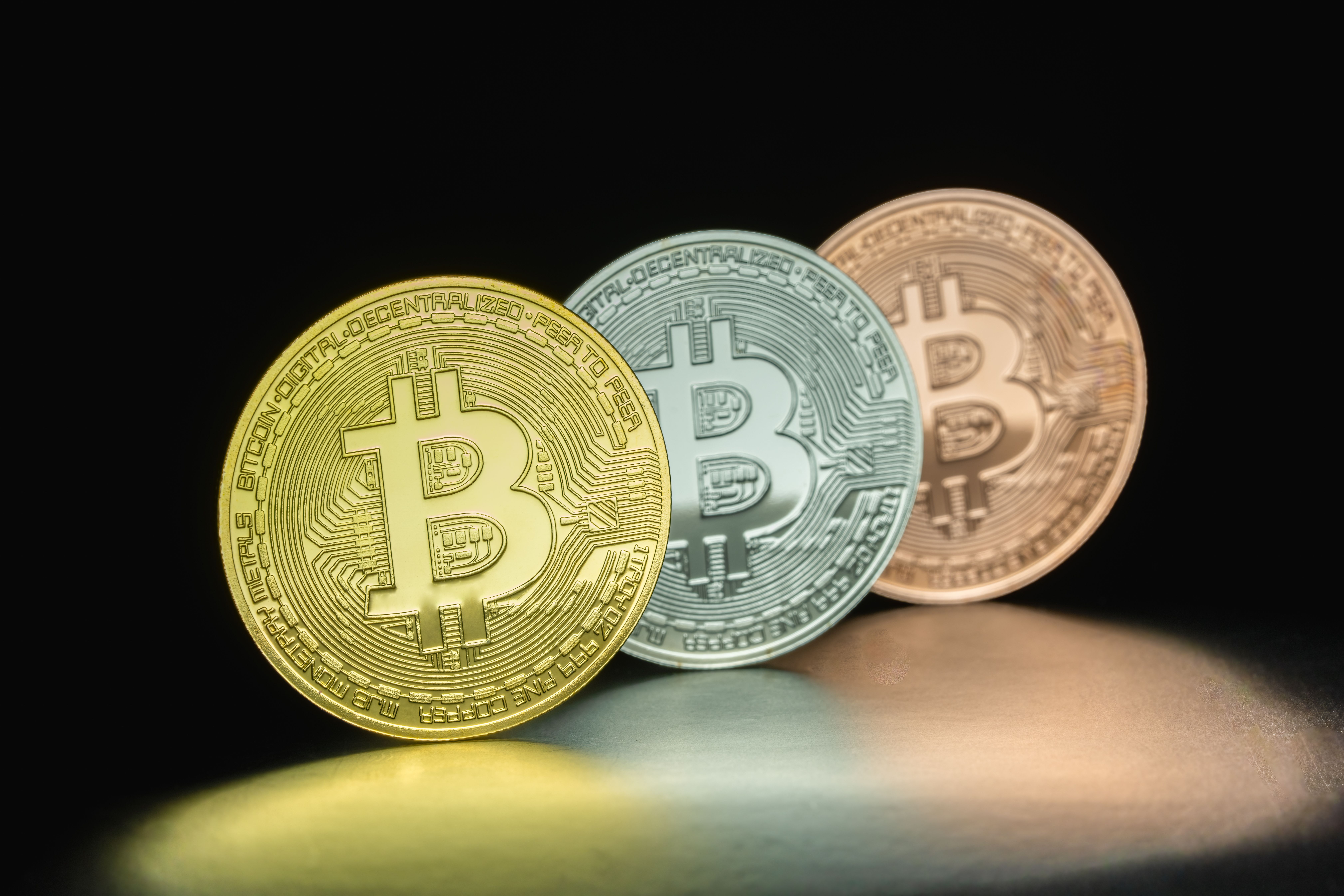 Close-up of three Bitcoin coins in dramatic lighting, symbolizing cryptocurrency investment and fintech innovation.