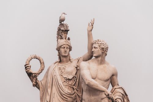 Free Statues of ancient Roman figures with a seagull perched on top, set against a cloudy sky. Stock Photo