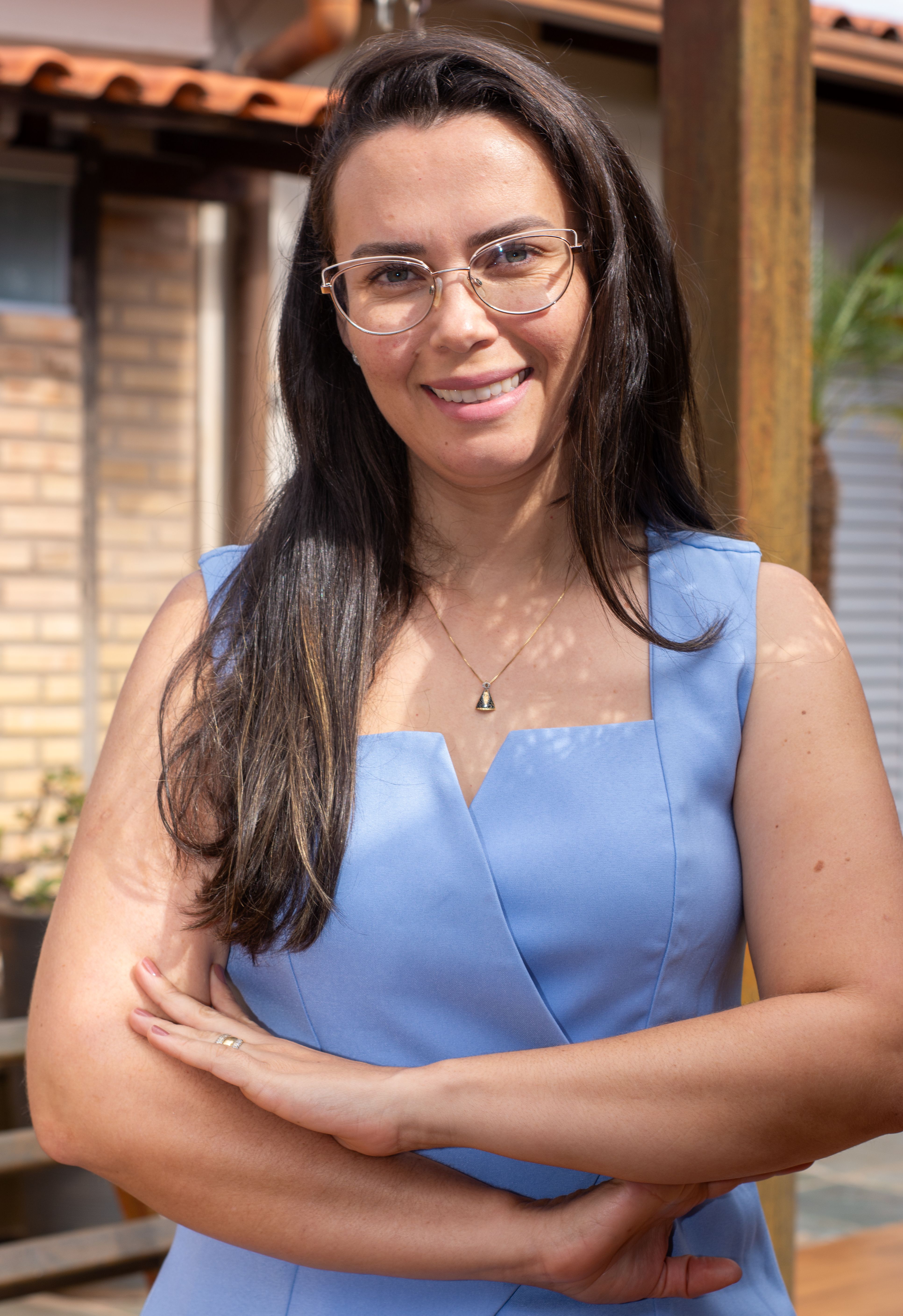 A smiling woman in a blue dress, posing outdoors with crossed arms, conveys confidence.
