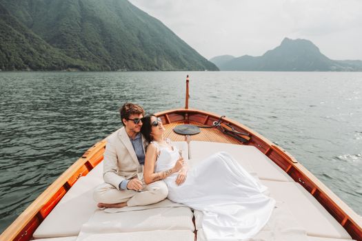 Elegant couple enjoys a serene boat ride on a picturesque lake surrounded by mountains.