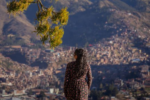 A woman in a floral dress gazes over the beautiful cityscape of Cusco, surrounded by mountains.