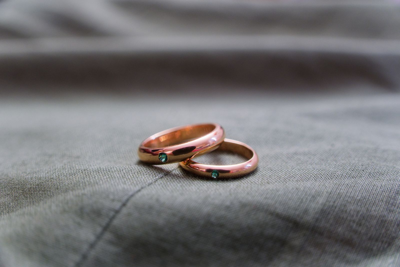Alliances en or rose ornées d'émeraudes sur un tissu gris