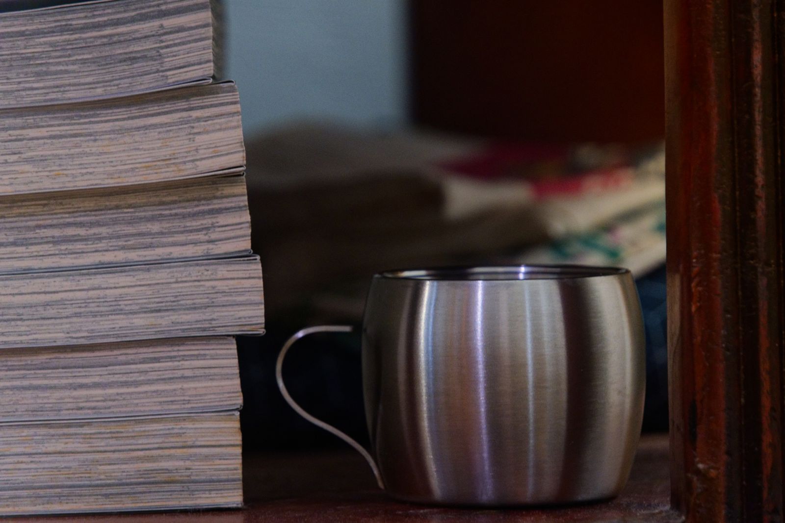 Pile de livres et tasse en inox sur une étagère en bois