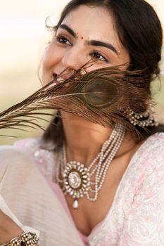Smiling woman adorned with jewelry and holding a peacock feather.