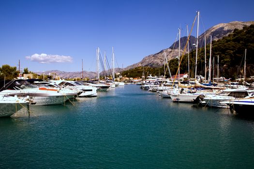 Idyllic marina scene in Krvavica, Croatia, with yachts and mountains under a clear blue sky.