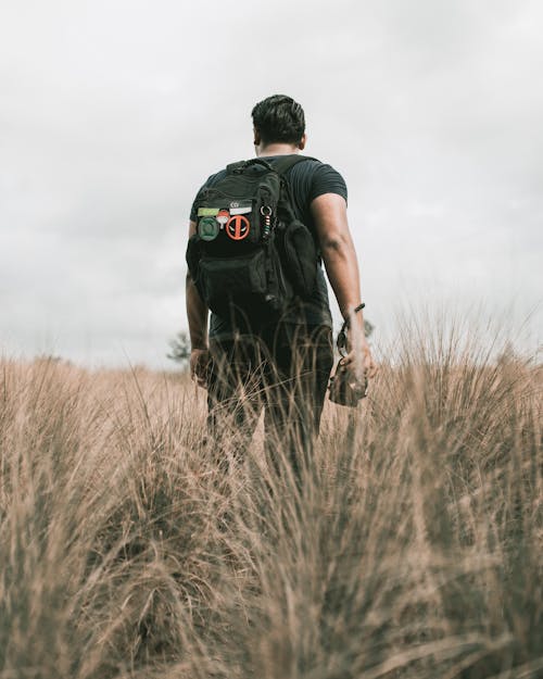 Man in Black T-shirt and Black Backpack Standing on Brown Grass Field